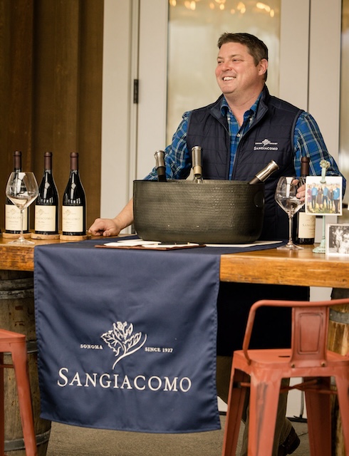 Andrew hosting the outdoor bar with bottles of wine smiling at the group