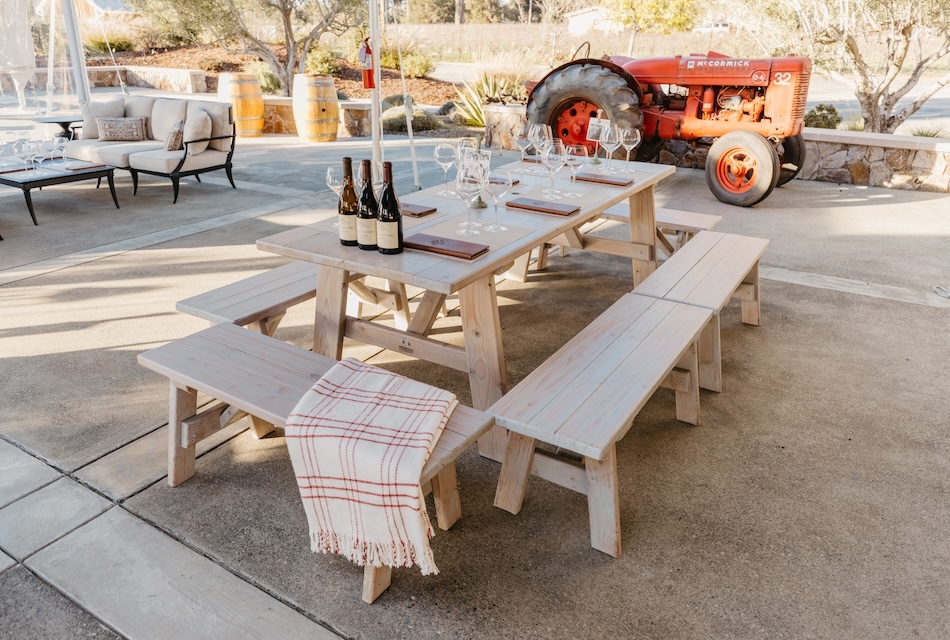 Pinic table on the terrace at Sangiacomo with a cozy blanket on the bench and bottles of wine on the table,.